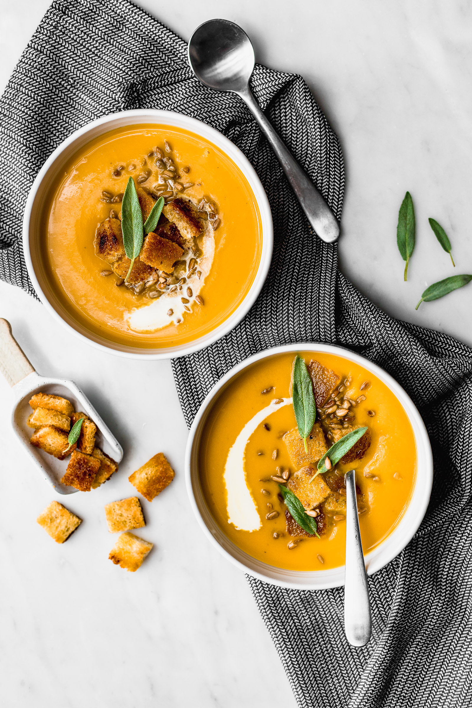 Two dishes of pumpkin soup with ginger, topped with croutons and sunflower seeds