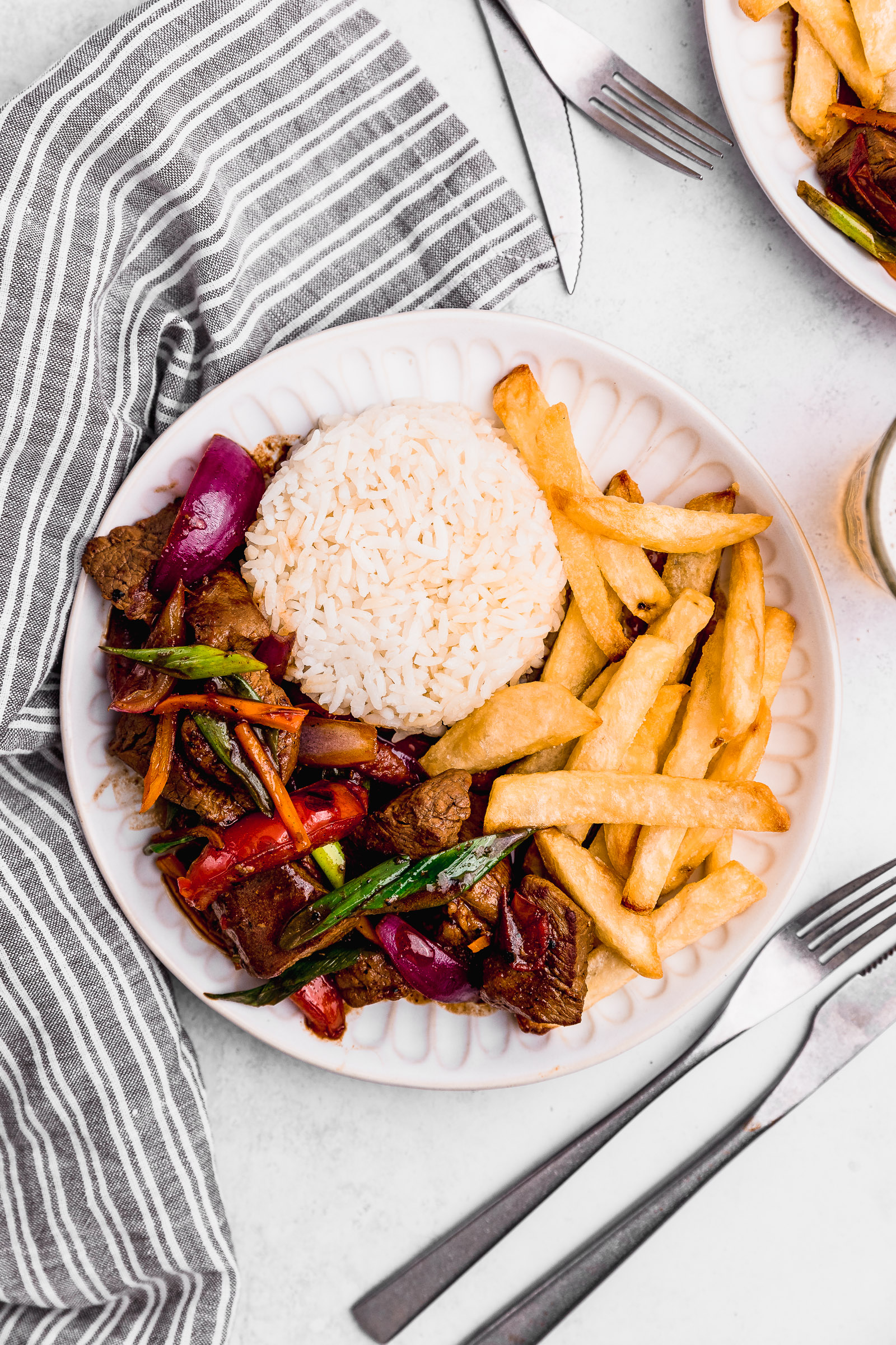 Top view of a dish of Peruvian lomo saltado. In the dish there's white rice, fries and the lomo saltado.