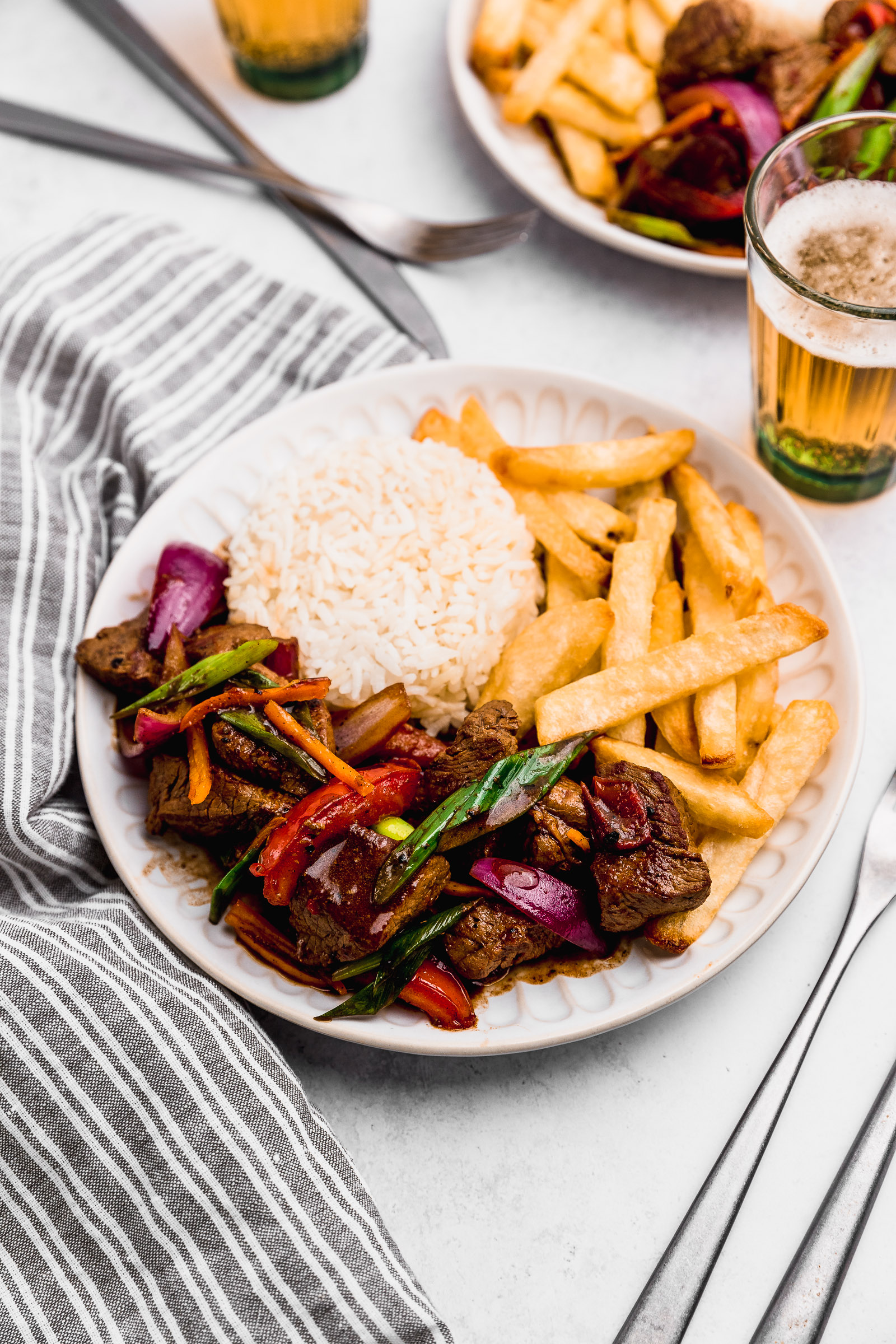 Closeup of a dish of Peruvian lomo saltado. In the dish there's white rice, fries and the lomo saltado.