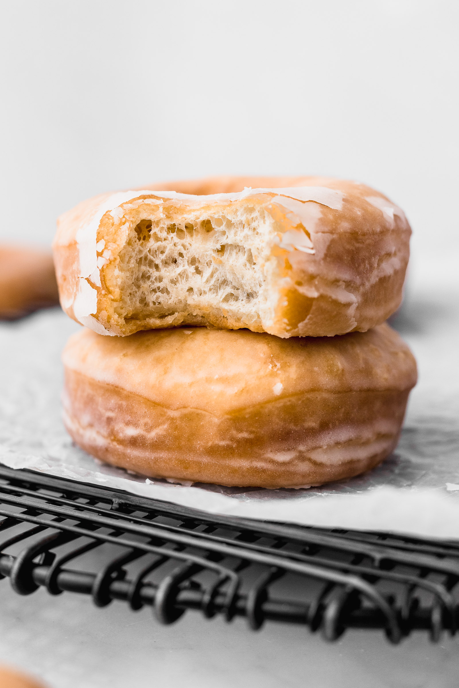 Closeup of a round glazed donuts with a shiny sugar exterior. A bite has been taken off and you can see the glaze breaking and the fluffy interior.