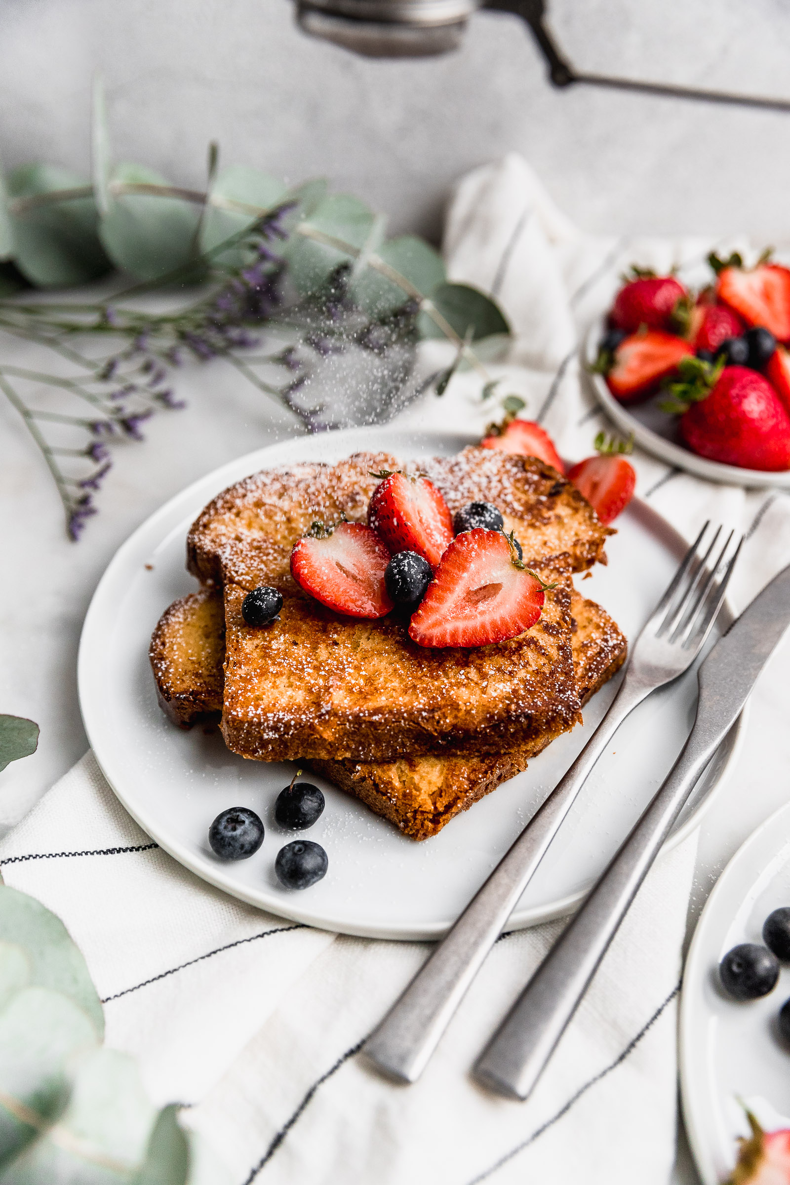 Dusting of icing sugar on brioche french toast with berries
