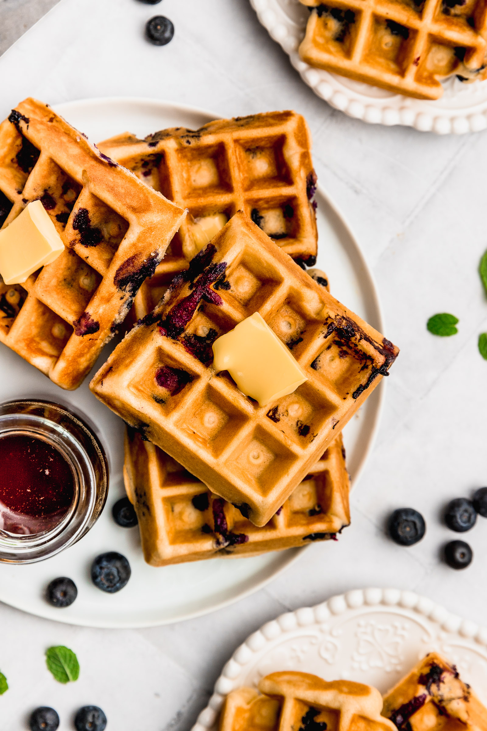 Closeup of blueberry waffles with a cube of butter and maple syrup on the side