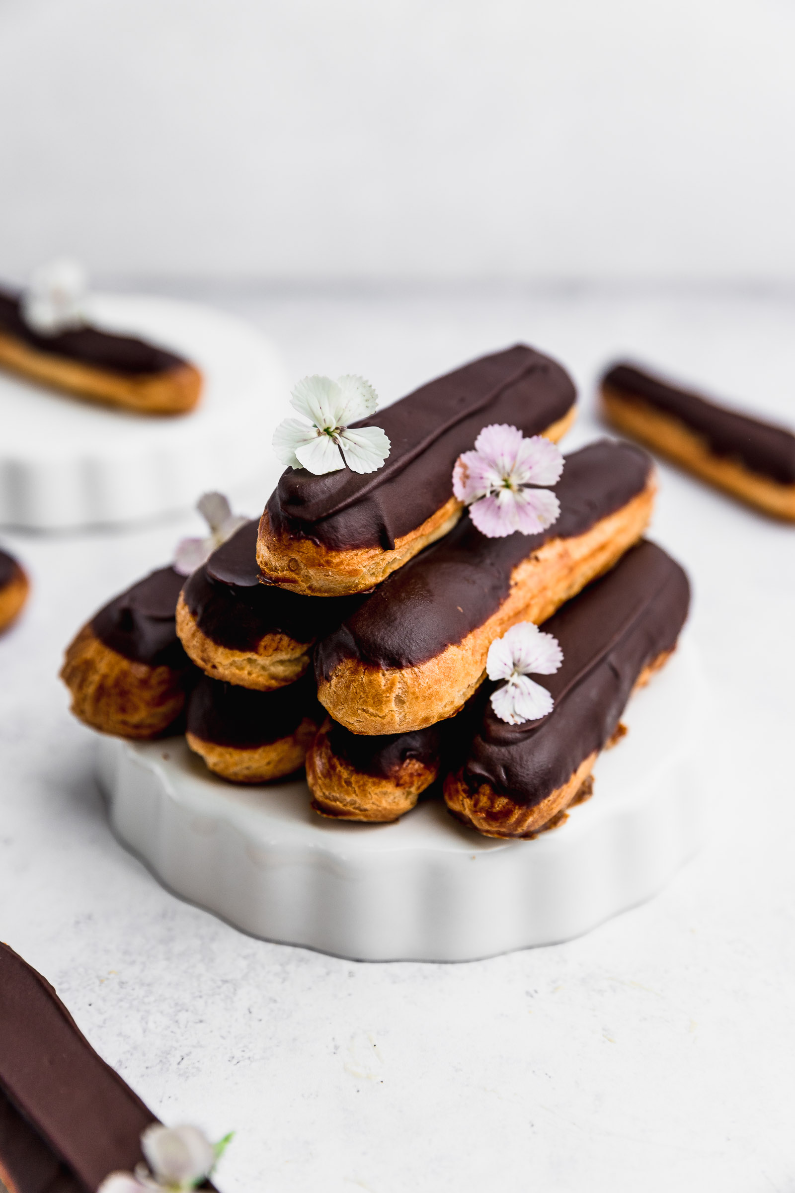 A pyramid of chocolate éclairs with for in the bottom, two on the second layer and one on top. There are also light pink edible flowers on them.