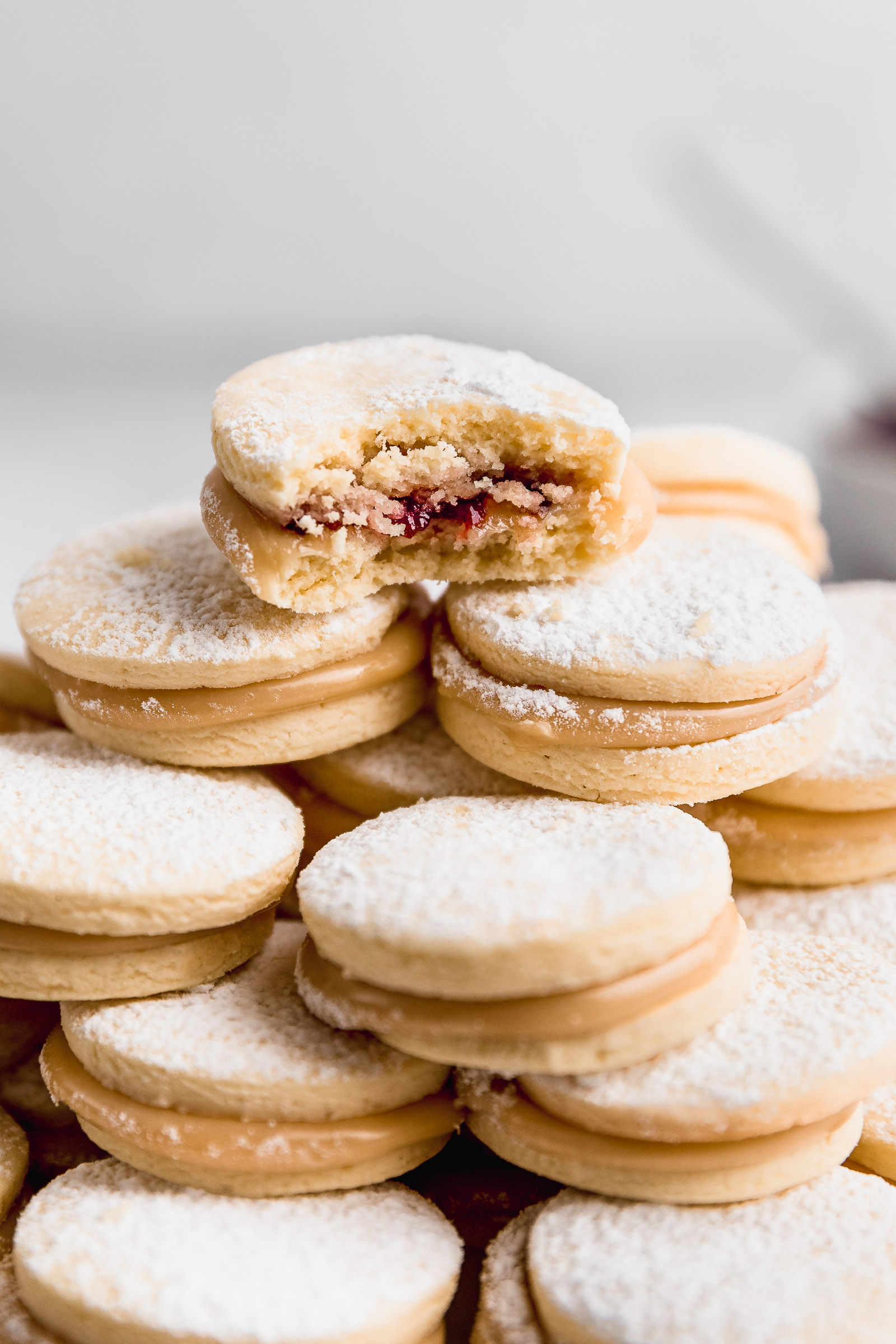 closeup of a tower of raspberry alfajores, at the top, one was bitten so you can see the raspberry marmalade centre