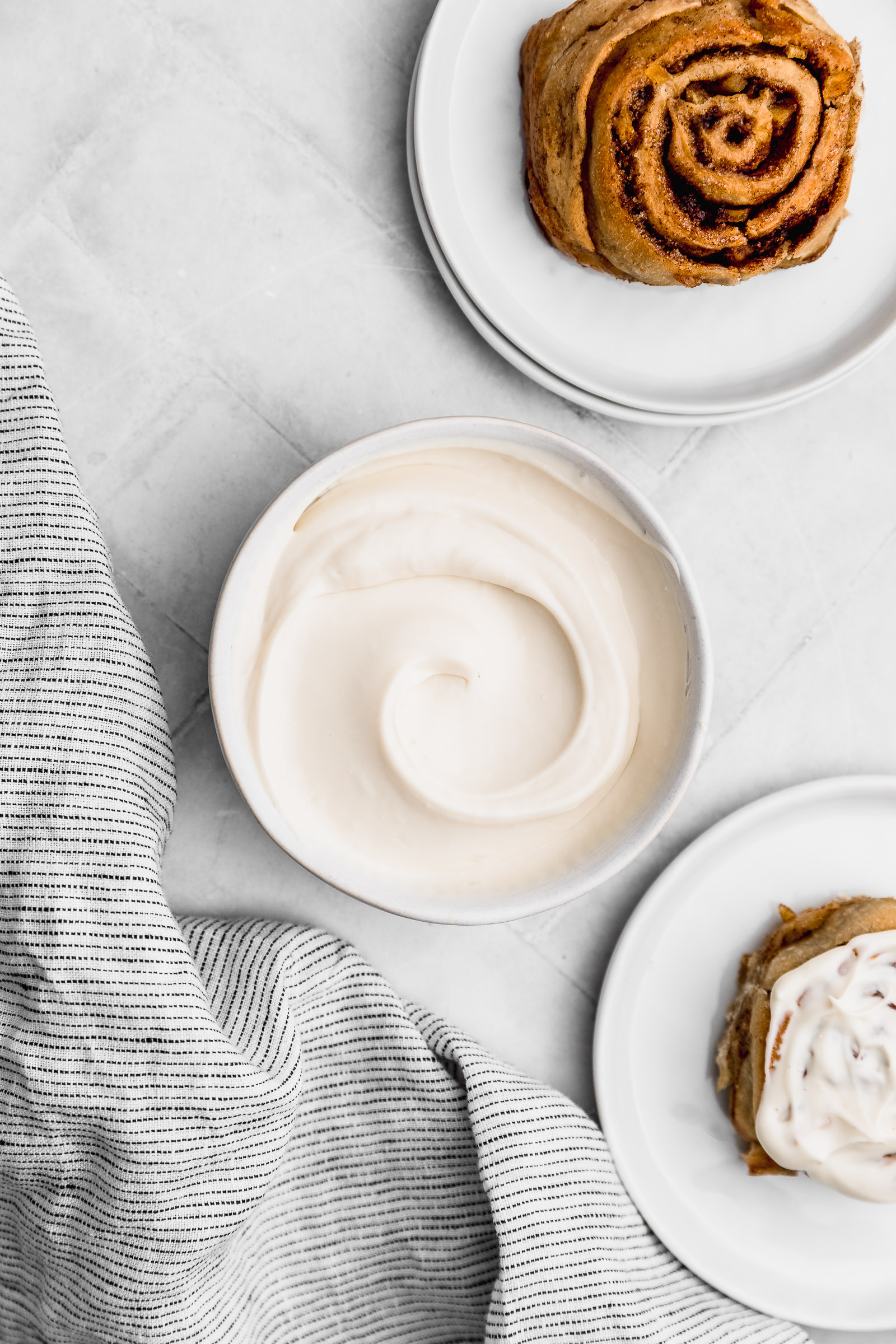 Bowl with cream cheese frosting for cinnamon rolls, with two cinnamon rolls peaking into the photo.