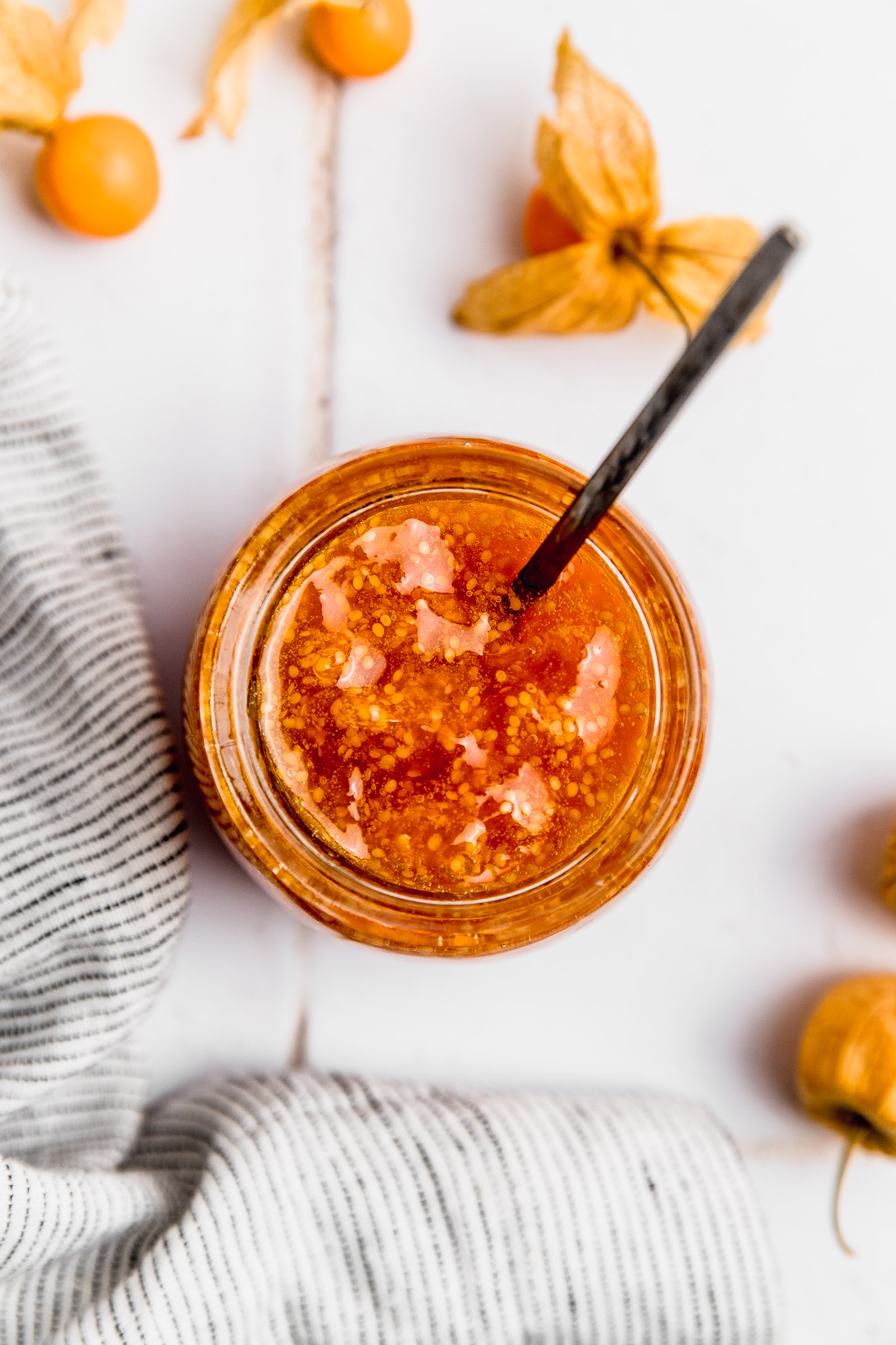 Closeup of Golden Berry Jam (Physalis Jam) in a glass jar with a spoon inside. You can see the seeds and shiny texture.