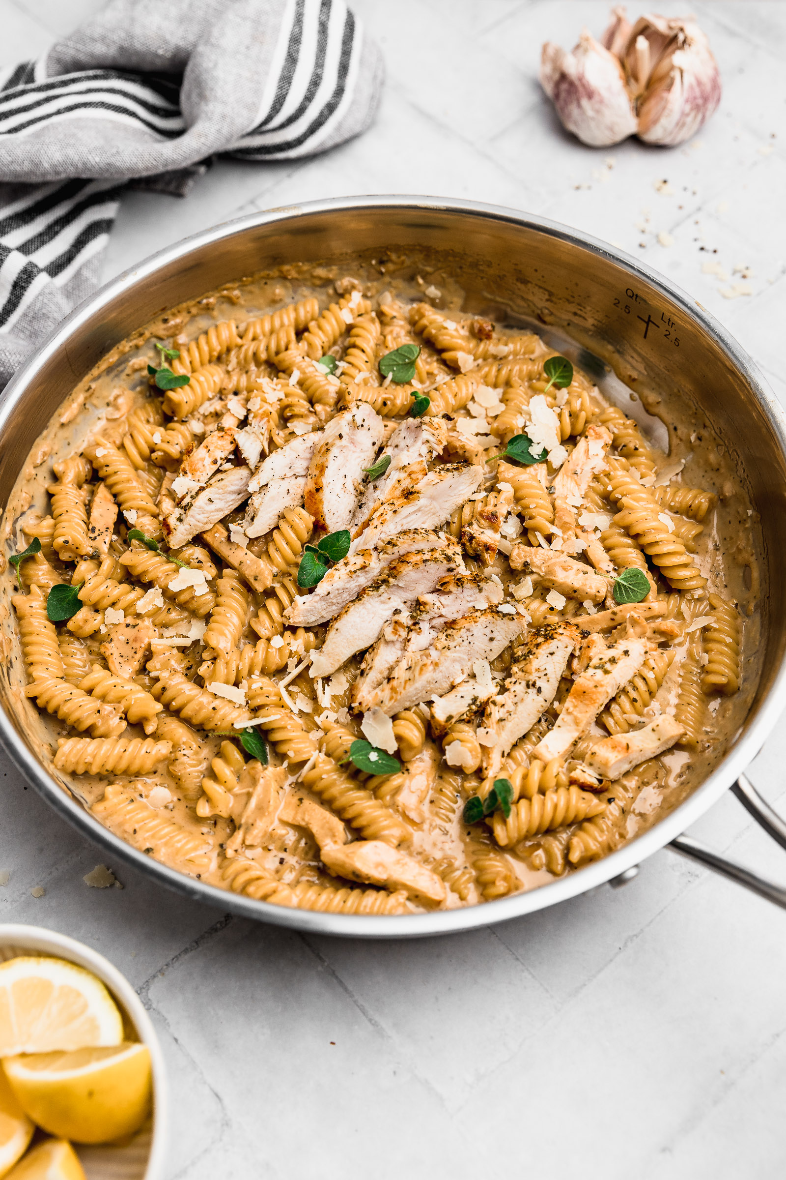Picture of Garlic Parmesan Chicken Pasta in the pan, where you can see the glossy and creamy sauce, as well as the golden chicken slices, fresh oregano leaves and parmesan flakes