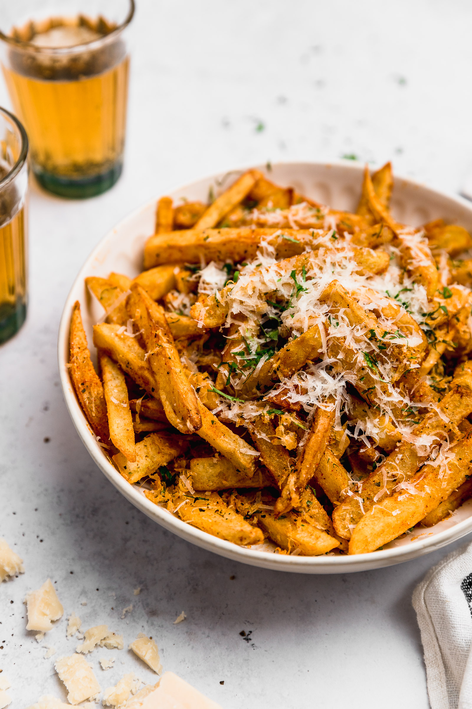 Close view of a bowl of Garlic Parmesan Fries, where you can see the grated parmesan, the colour of the spices and the chopped fresh parsley.