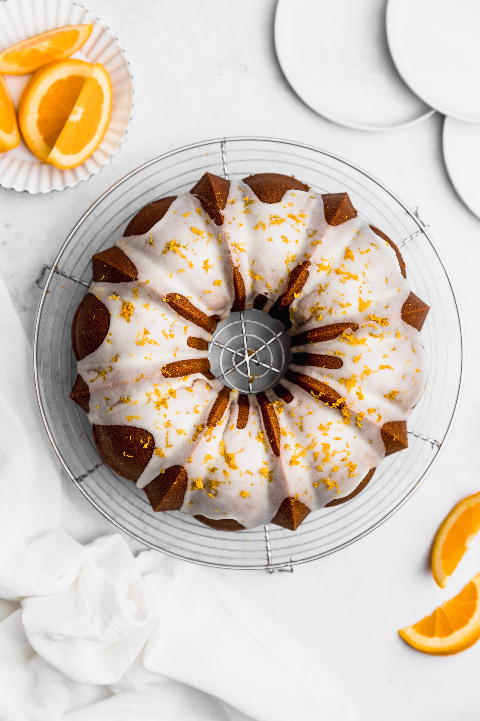Top View of a whole Orange Bundt Cake, with a white glaze and orange zest on top.