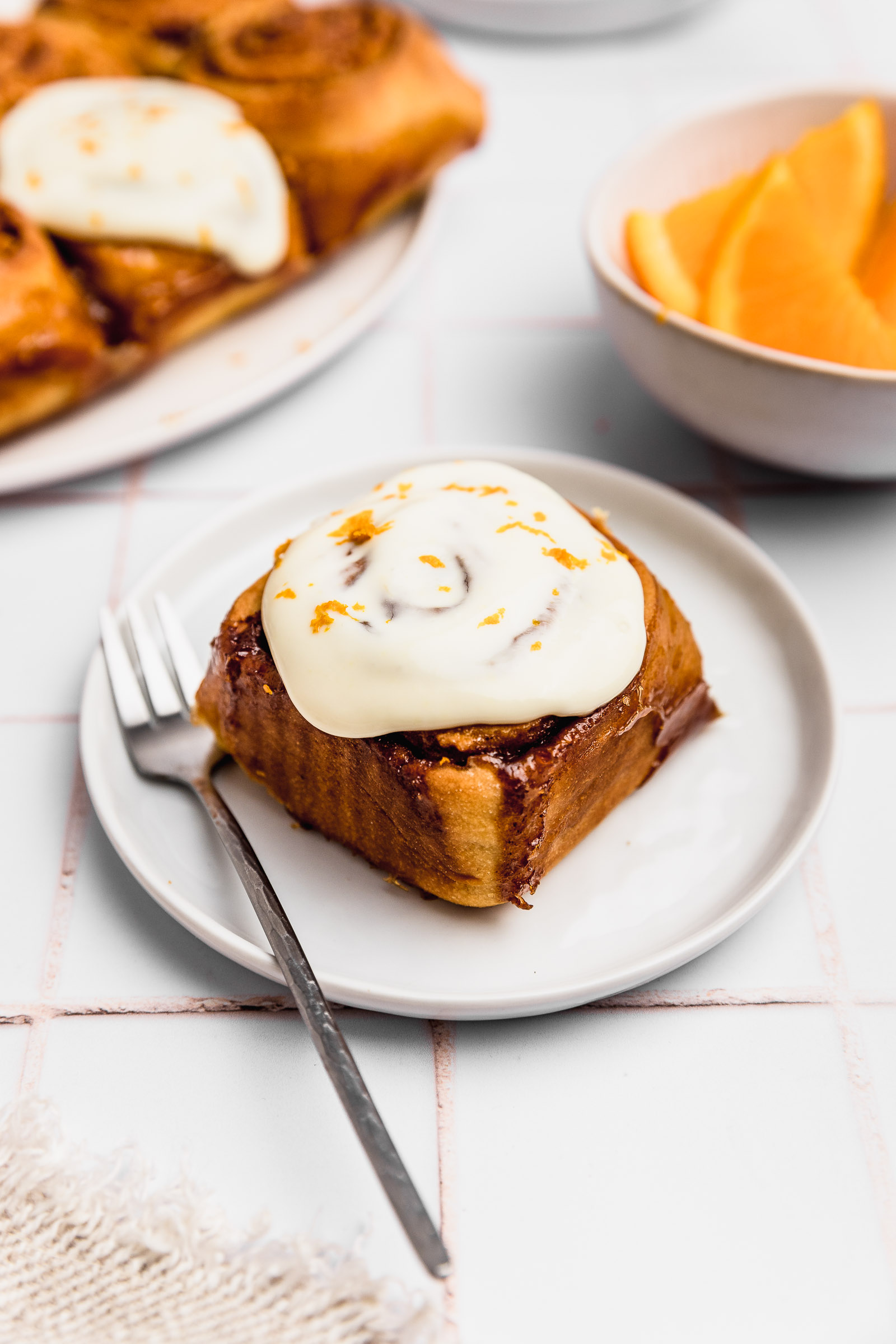 One single orange cinnamon roll with orange cream cheese frosting on top. It also has orange zest to finish.