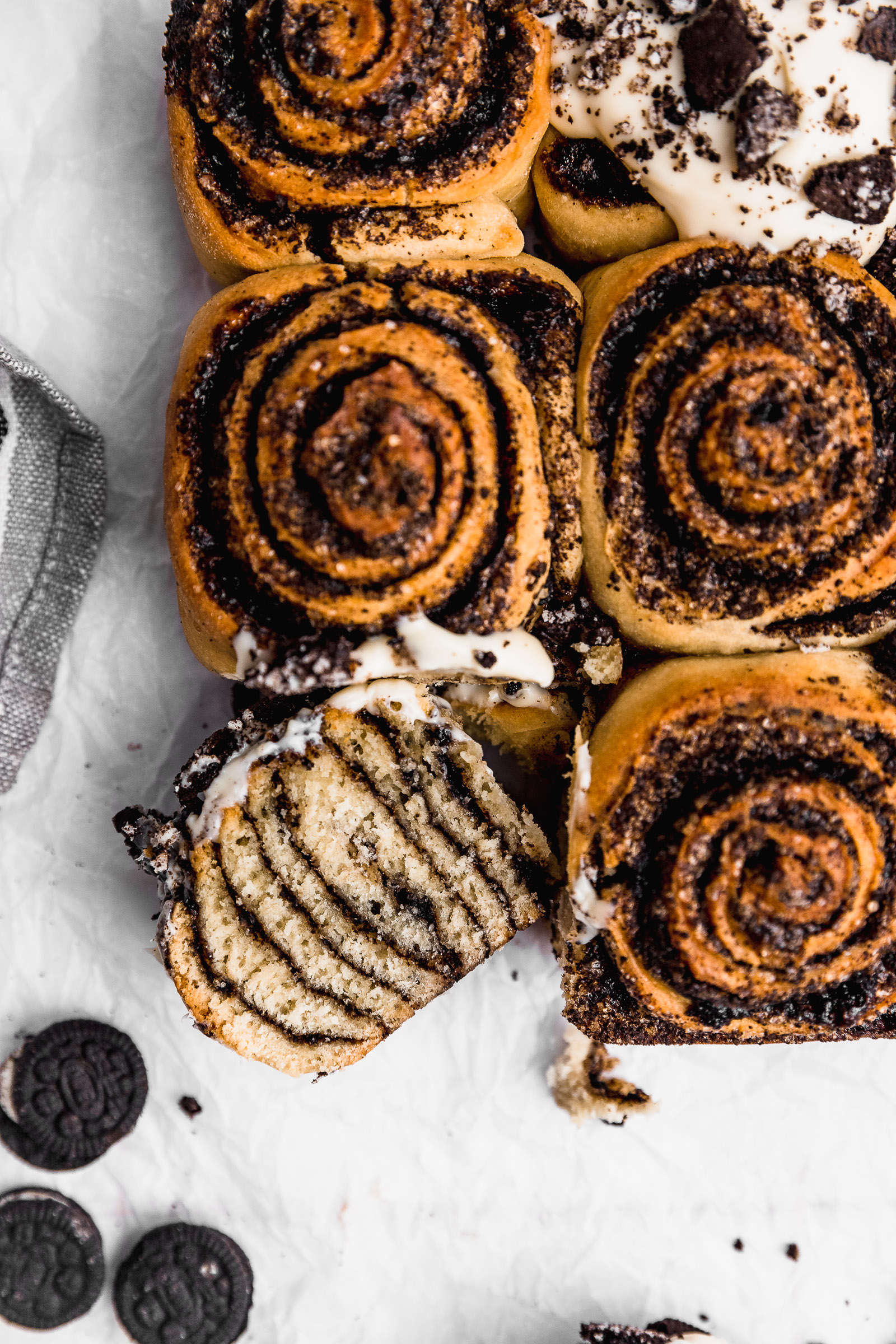 Top view of Oreo Cinnamon Rolls. One of them at the corner is cut in half and you can see the fluffy crumb as well as the black-coloured filling.