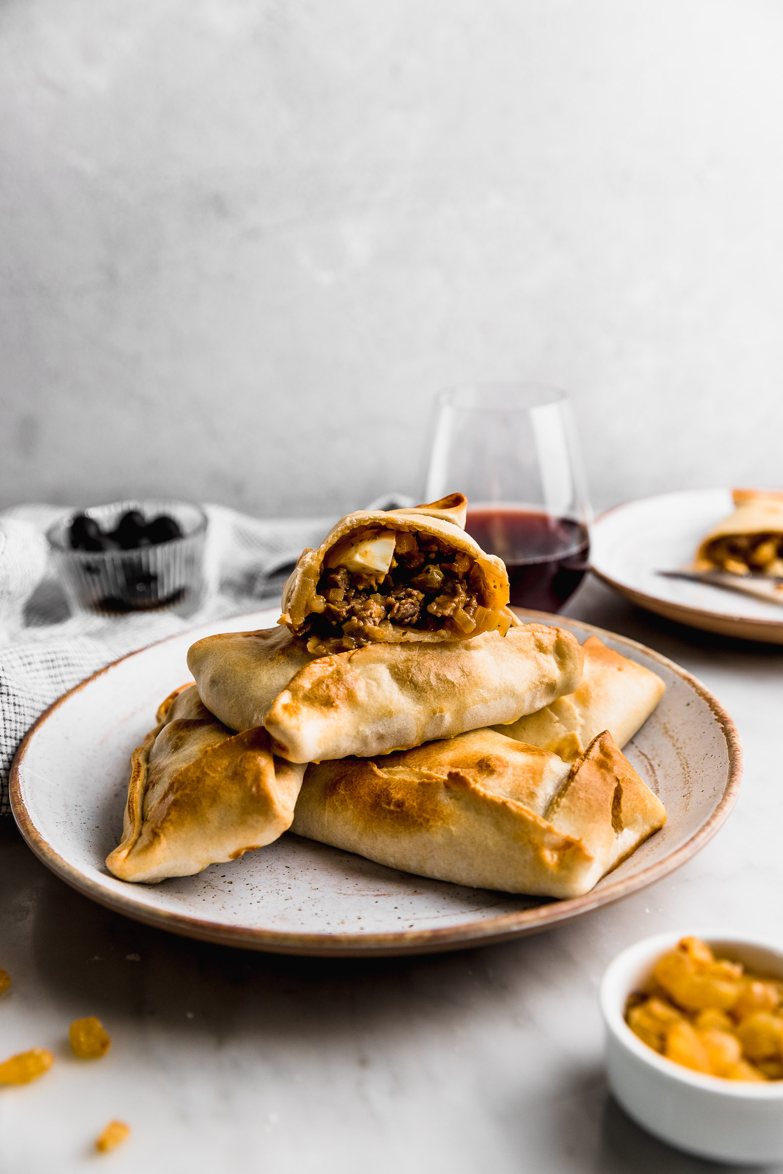 Photo of Chilean Empanadas (Empanadas de Pino). There are 5 empanadas forming a pyramid, and the one on top is cut in half so that you can see the filling of onion, beef, raisins and a quarter of a hard-boiled egg.