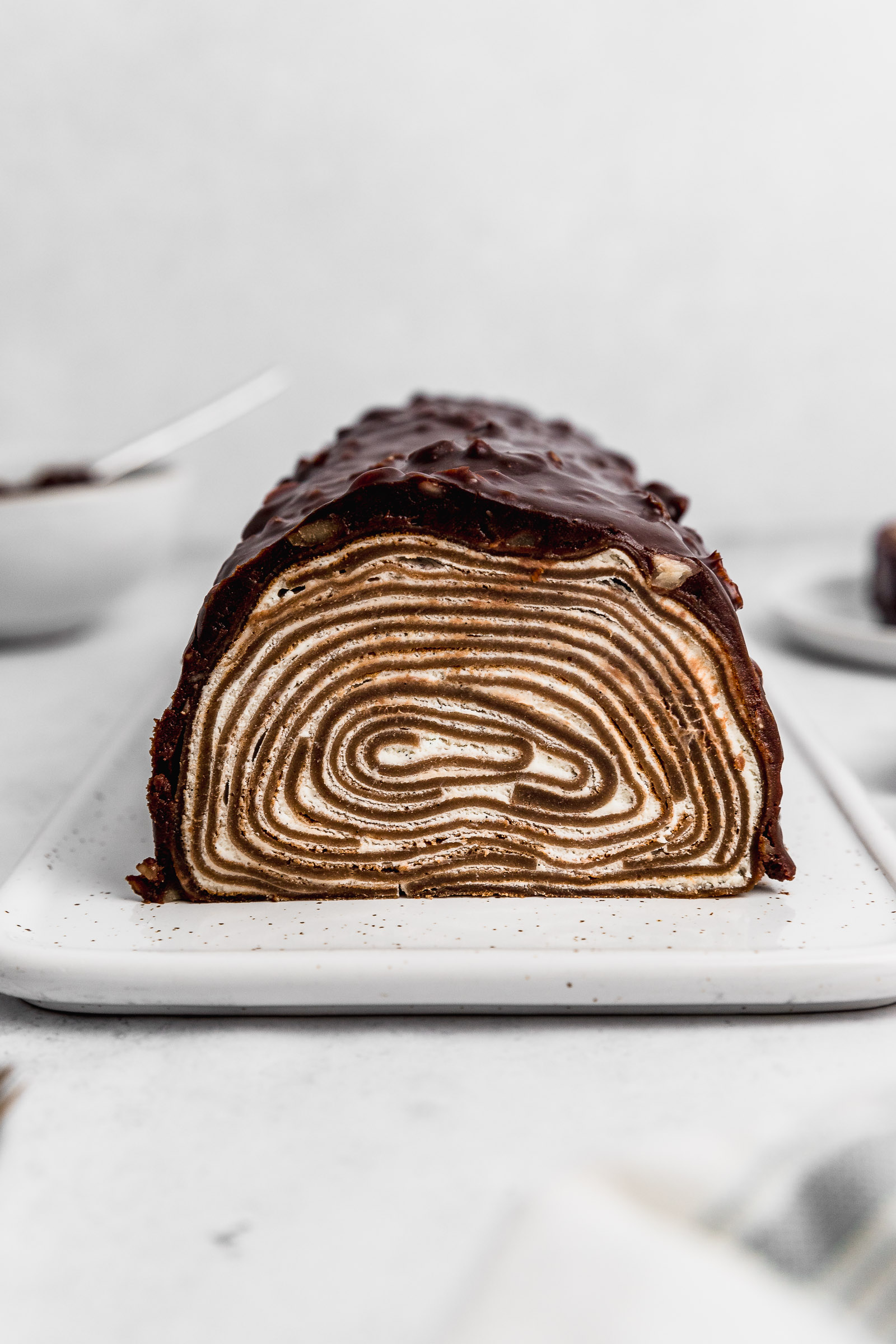Front view of a Chocolate Crepe Roll Cake Covered in Ganache. You can see the layers going around with a vanilla filling.
