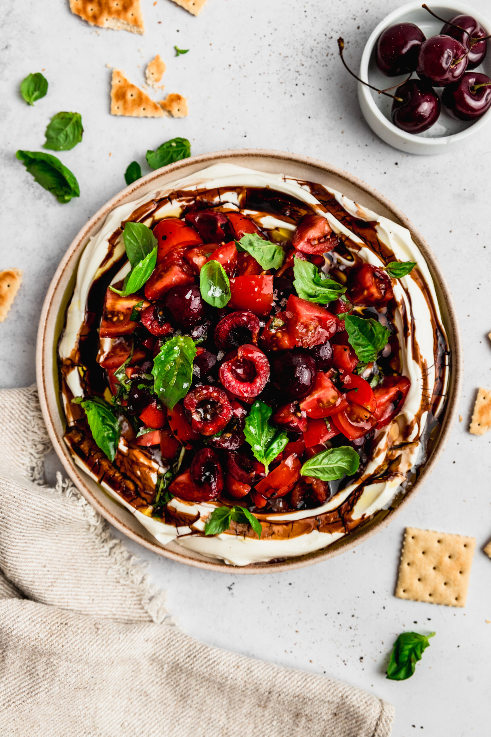 Top view of a cold caprese dip with fruit, in this case cherries. It's topped with fresh basil and finiched with a drizzle of olive oil and balsamic glaze.